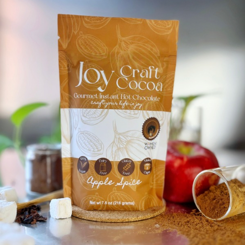 Bag of Joy Craft Cocoa Apple Spice 7.6 Ounce with an apple next to it and spilled cocoa